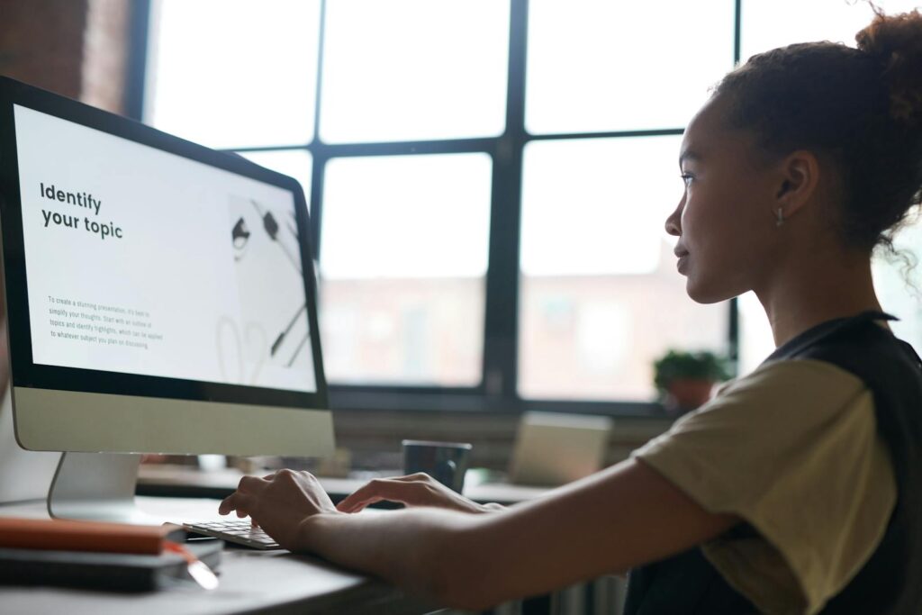 A woman attentively working on a computer in an office setting, focused on a presentation screen.